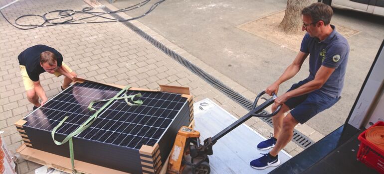 Zwei Menschen laden eine Palette mit Photovoltaik-Anlagen für den Balkon ab